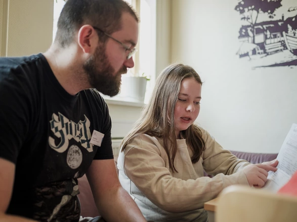 Ein Mann und ein Mädchen sitzen zusammen in einem gemütlichen Raum, lesen und diskutieren ein Stück Papier.