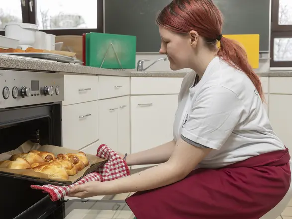 Auszubildende in der Hauswirtschaft holt frische Backwaren aus dem Ofen